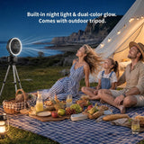 Outdoor family picnic scene at night under a stringed canvas tent, with a man, woman, and child sitting on a blue-and-white check blanket. A tripod-mounted fan on the left projects a bright circular light beam toward the sky.