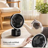 A small black handheld fan with a circular white trim is shown in a bright living room next to a gray-and-white cat. A human hand is touching the fan, and a text banner at the bottom says 'Pinky-safe certified.