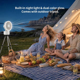 A family picnic outdoors at night under a string-tent canopy, with a portable white projector fan on a tripod casting a bright light beam across the sky. Text at the top reads, 'Built-in night light & dual-color glow.
